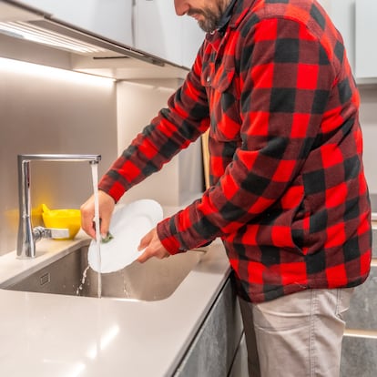 Unrecognizable man washing dishes with hot water and soap at home in the kitchen. Everyday moments of coexistence and cleaning the house