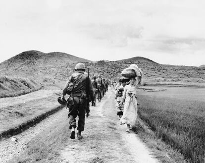 American soldiers pass by a group of Korean refugees, on their march to the Naktong River region, in August 1950.
