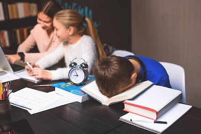 Un alumno duerme sobre un libro en una biblioteca.