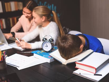 Un alumno duerme sobre un libro en una biblioteca.