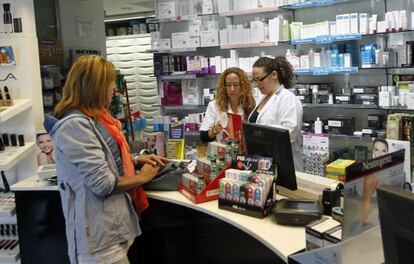 Dos empleadas de la farmacia licenciada Elena Timpanaro, en Bilbao, atienden a una clienta.