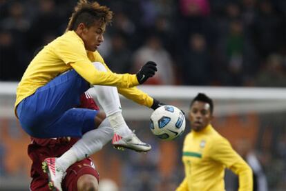 El delantero brasileño Neymar trata de controlar el balón en una postura acrobática ante un defensa venezolano. Al fondo, Robinho.