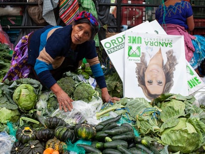 Una vendedora junto a una imagen publicitaria en un mercado de Guatemala.