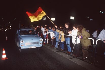Un conductor de un Trabant, un vehículo de bajo coste de la RDA, pasa por un punto de control del muro de Berlín mientras varios ciudadanos le animan.