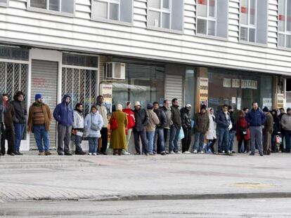 Varias personas forman una larga cola ante una oficina de empleo.