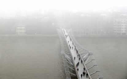 Un grupo de peatones camina sobre el Puente del Milenio de Londres (Inglaterra), rodeado por la niebla.