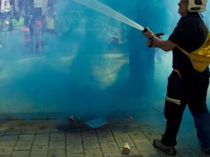 Un bombero riega a los manifestantes, envueltos en una cortina de humo.