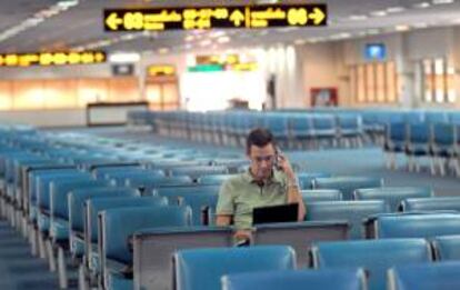 Un pasajero observa su ordenador y habla por el móvil en una sala vacía del aeropuerto Don Mueang de Bangkok (Tailandia). EFE/Archivo