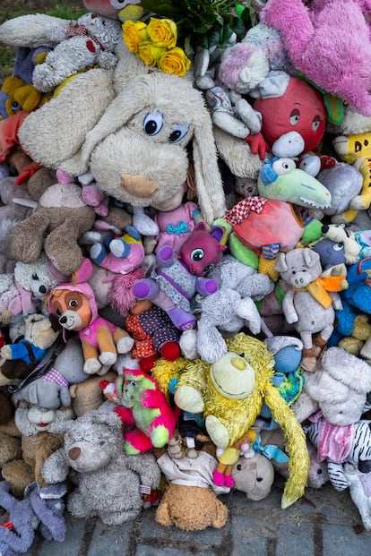 Animales de peluche apilados en una parada de autobús en Dnipró, frente a un edificio de viviendas destruido.