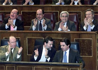 José María Aznar habla con Mariano Rajoy mientras es aplaudido por Rodrigo Rato y varios diputados del Partido Popular.