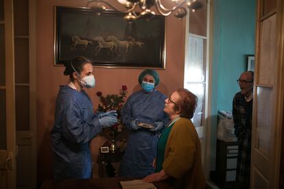 Las enfermeras Esther Caner y Cristina Menéndez conversan con Enrica Martinez (78 años) y Manolo Ortiz (79 años) en el comedor de su vivienda durante una visita.