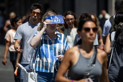 Una mujer se protege del sol con la ayuda de un cartón mientras cruza un paso de zebra de plaza Catalunya, en Barcelona.