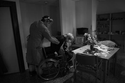 Uno de los sanitarios ayuda a una posible enferma nonagenaria a colocarse en una silla de ruedas para trasladarla al hospital.