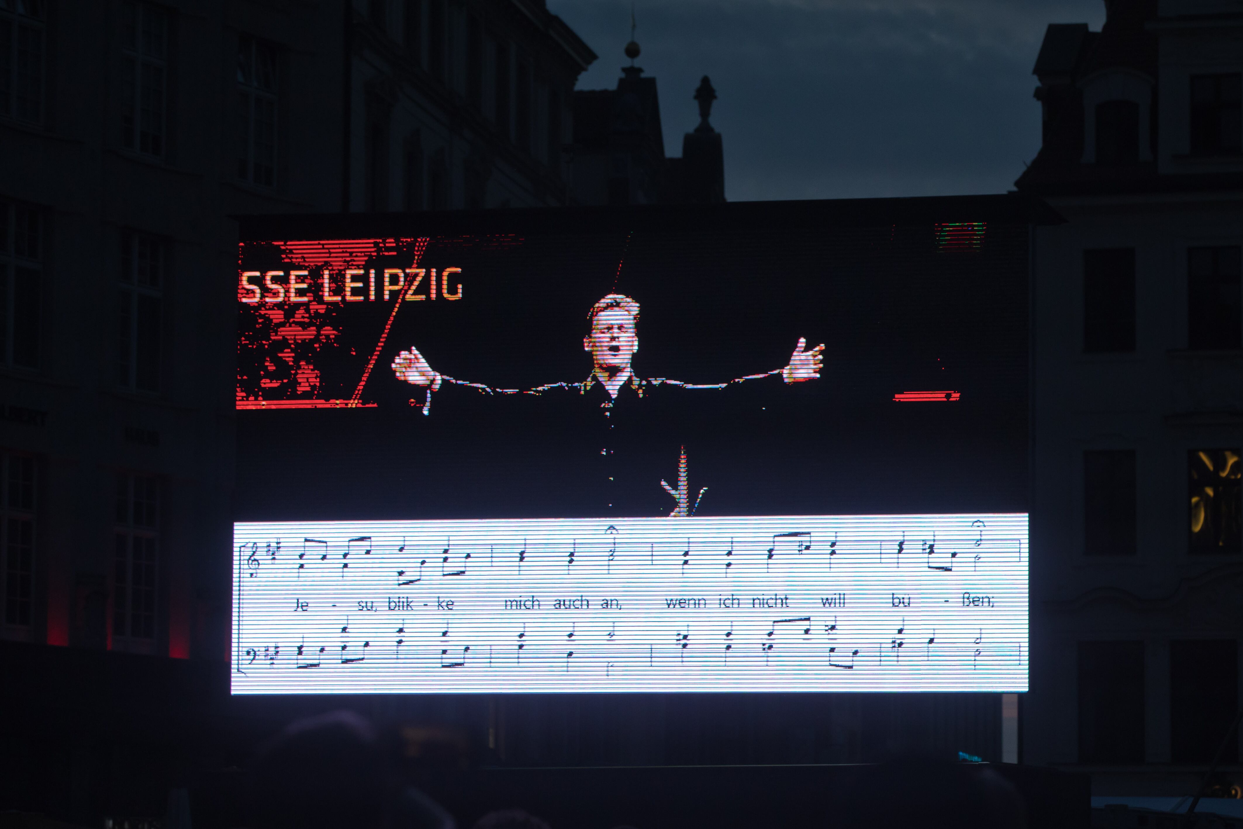 En una pantalla se proyectaban los textos y la música de los corales para que pudieran cantarlos los asistentes al concierto de la Marktplatz.