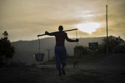 Un hombre transporta cubos de agua por una calle de Santiago cuando cierran los establecimientos turísticos y la ciudad se queda a oscuras y en silencio. Los expertos auguran un buen futuro turístico para Santiago de Cuba tras el eventual levantamiento del embargo con EE UU.