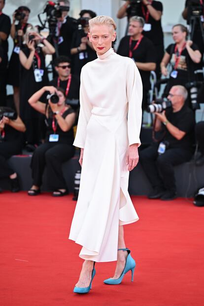 Tilda Swinton, una elegancia de otro planeta. La actriz, conocida por su estilo andrógino y ecléctico, destacó en el estreno de 'Queer', la nueva película de Luca Guadagnino, durante el Festival de Venecia 2024. La actriz lució un llamativo conjunto blanco compuesto por un vestido de seda con cuello alto y diseño asimétrico de Loewe, combinado con unos zapatos de salón turquesa con pulsera al tobillo de Maison Alaïa, modelo Decollete. Su elección reafirma su capacidad para fusionar elegancia y originalidad en la alfombra roja.