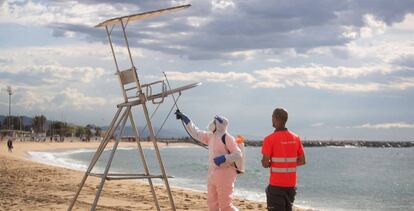 Unos trabajadores desinfectan los puestos de socorrismo en la playa del Bogatell.