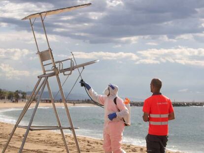 Unos trabajadores desinfectan los puestos de socorrismo en la playa del Bogatell.