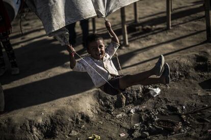 Un niño se columpia con la lona que cubre una de las tiendas comunes del campamento de refugiados.