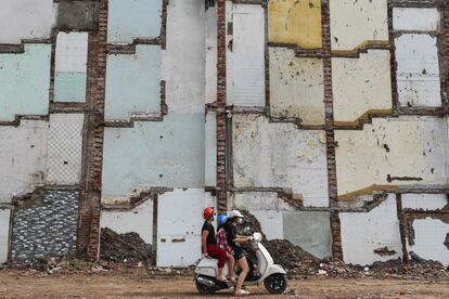 Varios ocupantes de una moto, con mascarilla, circulan por una zona residencial que se demolirá para la construcción de una carretera en Hanói (Vietnam).