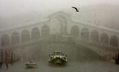 Una lancha pasa envuelta en la niebla bajo el puente del Rialto en el Gran Canal de Venecia.