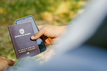 Una persona sostiene un pasaporte colombiano y un teléfono inteligente.