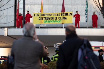 Cuatro miembros de la organización subidos al tejado de la entrada de El Corte Inglés, sujetan una pancarta con el mensaje de: "Los combustibles fósiles destruyen el clima". El cuerpo de bomberos y dos peatones lo ven desde la acera. Imagen distribuida por la ONG.
