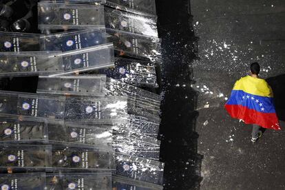 Um manifestante passa com a bandeira venezuelana em frente os policiais.