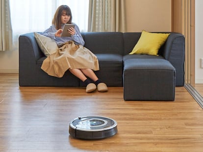 Una mujer está sentada en su casa mientras un aspirador de la marca iRobot limpia su sala.