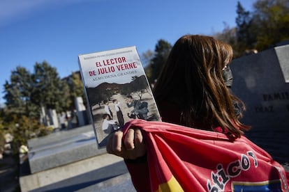 Una mujer con un libro de Almudena Grandes y una bandera del Atlético de Madrid asiste al entierro de la escritora en el cementerio de la Almudena.