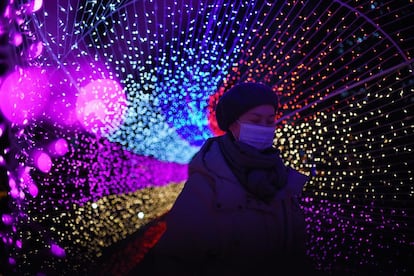 Una mujer camina con una máscara por un camino iluminado con luces multicolores en Pekín (China). 