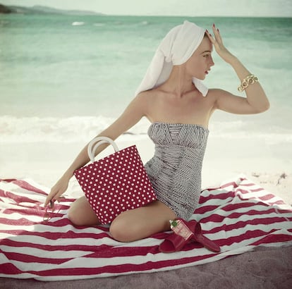 Model seated on striped beach towel wearing grey and white patterned strapless bathing suit. (Photo by Roger Prigent/Condé Nast via Getty Images)