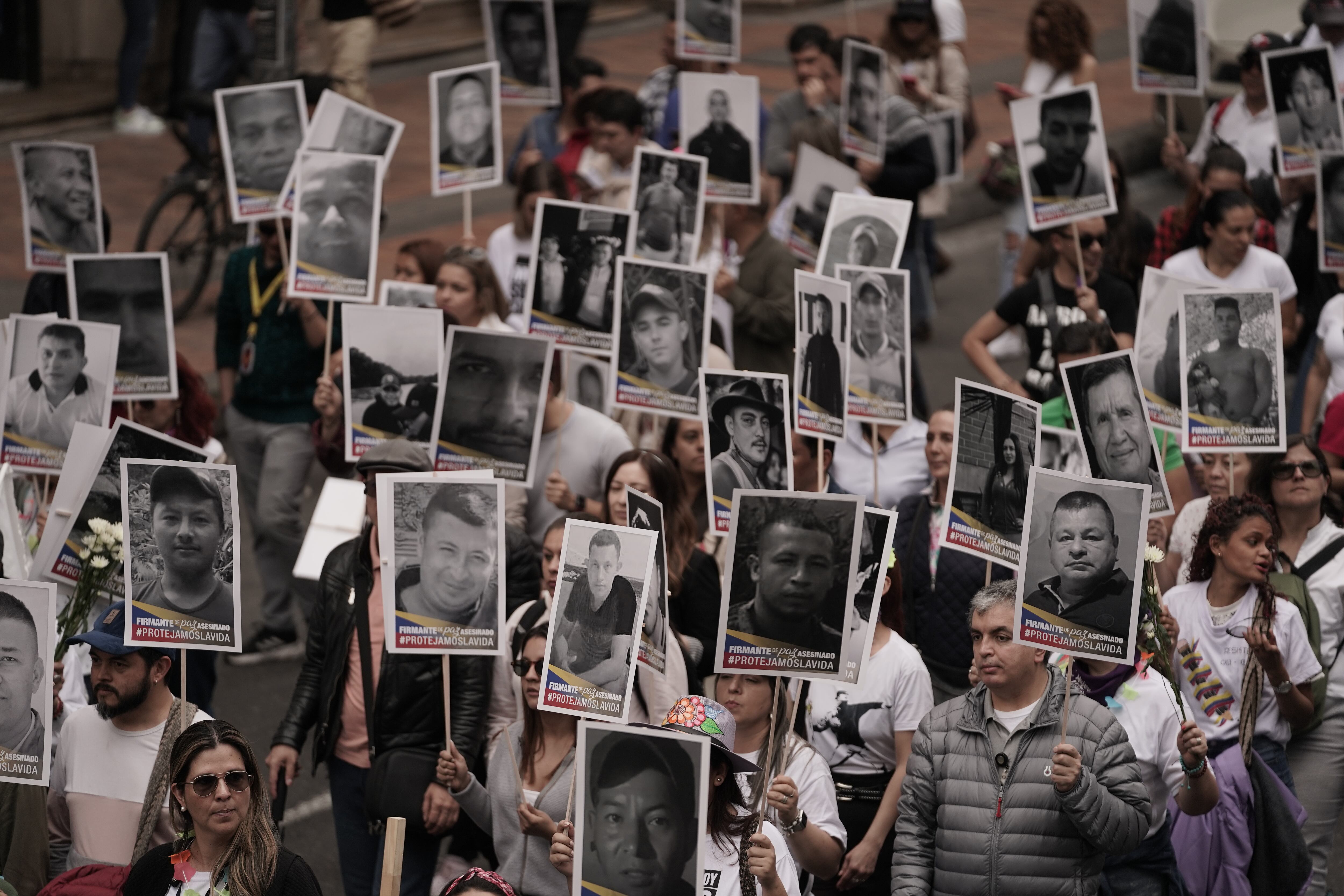 Manifestantes sostienen fotografías de firmantes de paz que han sido asesinados en Colombia.