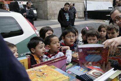 Un grupo de niños observa un libro en los puestos instalados en la plaza de Sant Jaume de Barcelona. La ciudad vive una jornada de rosas y libros. Decenas de autores firman sus obras en librerías y tenderetes callejeros