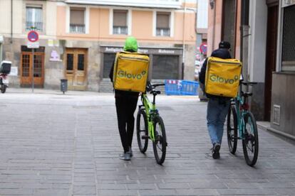 Dos repartidores de Glovo empujan sus bicis por la calle.