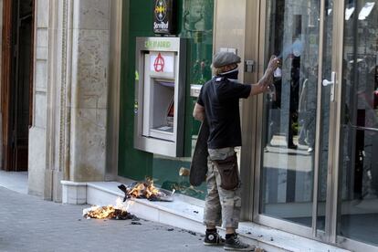 Un manifestante pinta con un spray la puerta de una entidad bancaria del paseo de Gràcia de Barcelona.