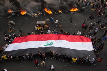 Manifestantes iraquíes llevan una bandera nacional gigante mientras otros queman neumáticos en la ciudad de Basora, en el sur del país.