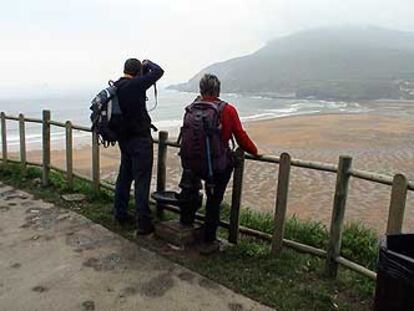 Dos peregrinos disfrutan con la vista de la playa de La Arena, en Zierbena (Vizcaya), en un tramo del Camino del Norte que discurre en este punto por una antigua vía de ferrocarril reconvertida en senda.