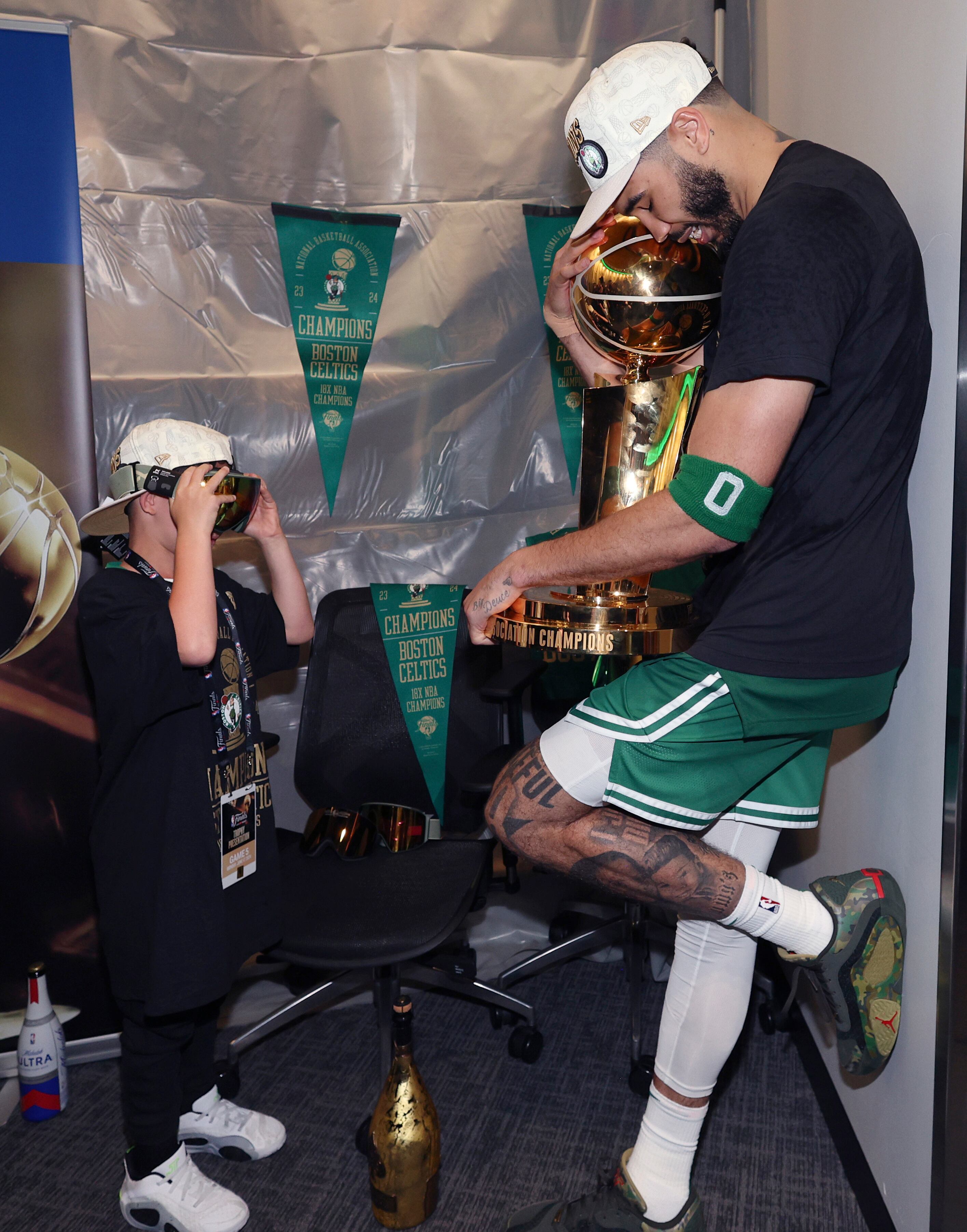  Jayson Tatum abraza el trofeo mientras su hijo Deuce le toma una fotografía. 