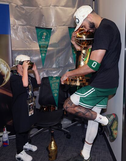  Jayson Tatum abraza el trofeo mientras su hijo Deuce le toma una fotografía. 