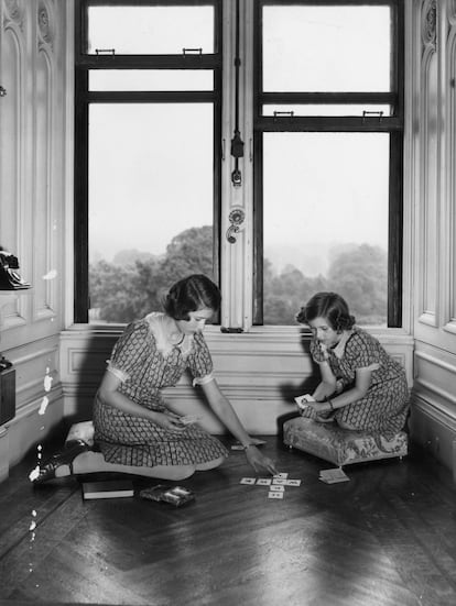 <p>Hay una inquietante simetría en esta imagen de Lisa Sheridan que es puro pictorialismo fotográfico: Elisabeth y Margaret juegan a las cartas en un pasillo del Royal Lodge de Windsor en 1940. Van vestidas y peinadas de forma similar, cada una está apostada bajo una ventana y Margaret se ha subido a un escabel para no descompensar la imagen.</p>