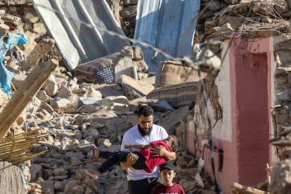 Un hombre camina junto a sus hijos entre los escombros de varias viviendas, en Tafeguagut.