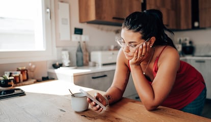 Una mujer revisa su smartphone en la cocina.