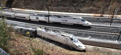 Un tren circula esta mañana por la vía paralela a la del accidente, donde siguen los restos del convoy siniestrado.