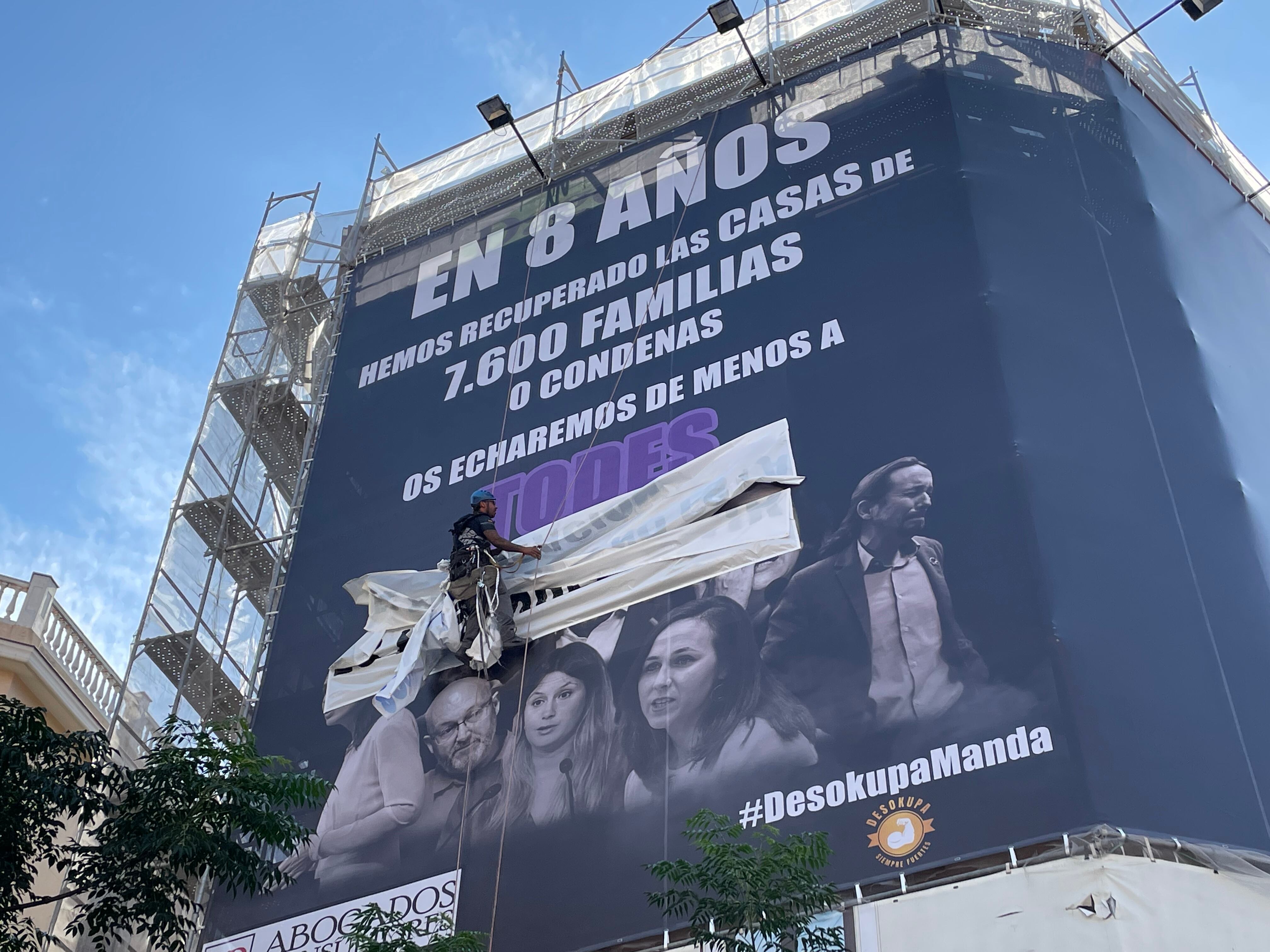 Un operario retira los carteles pegados por el Movimiento por la Vivienda de Madrid sobre la lona de Desokupa en la calle de Atocha. 