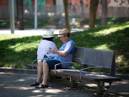Un hombre mira su teléfono móvil en un banco bajo la sombra de unos árboles en el parque de la Barceloneta, este miércoles en Barcelona.
