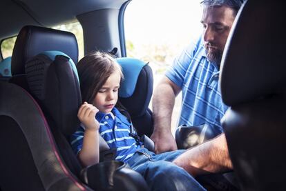 Un padre coloca en la silla del coche a su hija. 