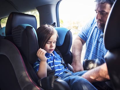 Un padre coloca en la silla del coche a su hija. 