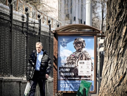 Un hombre pasa por delante de un cartel propagandístico colocado en una calle de Moscú en el que se lee "Nuestra profesión, defender nuestra patria".