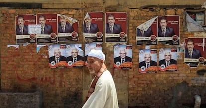 Un egipcio pasa por un muro con carteles electorales de Morsi (arriba) y Abulfut&uacute; (debajo) en este viernes en El Cairo.